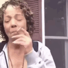 a woman is smoking a cigarette in front of a window with her eyes closed .