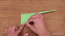 a person is holding a piece of green paper on a wooden table and the words made in animatica are visible