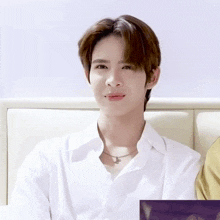 a young man wearing a white shirt and a necklace is sitting on a couch