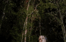 a woman is pointing a gun at the camera in a forest .