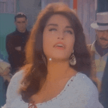 a woman with long hair is wearing a white shirt and earrings and a hat .