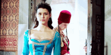 a woman in a blue dress stands next to a man wearing a red hat