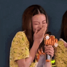 a woman in a yellow shirt is holding a microphone and covering her mouth with her hand .