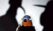 a stuffed bird with a blue head is standing in front of a shadow of a person