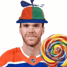 a man wearing a hat that has a propeller on it is holding a colorful lollipop