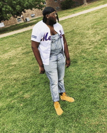 a man wearing overalls and a mets jersey is standing in the grass