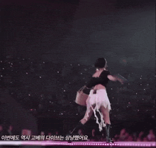 a woman in a black top and white skirt is dancing on a stage in front of a crowd
