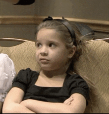 a little girl with her arms crossed and a black headband