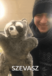 a man is holding a stuffed raccoon with the word szevasz written below him