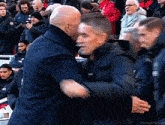 a man in a suit is hugging another man in a jacket in front of a crowd