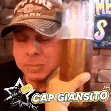 a man in a hat is holding a glass of beer and says cap giansito on the bottom