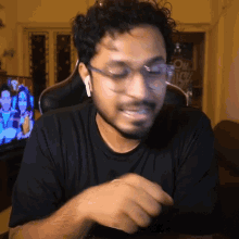 a man wearing glasses and ear buds sitting in front of a tv