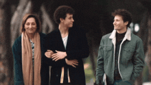 three people are walking down a street and one of them is wearing a green jacket