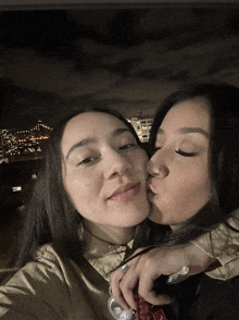 a woman kissing another woman on the cheek with a city in the background