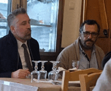 two men sit at a table with wine glasses