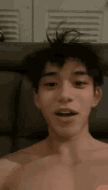 a shirtless young man is smiling and looking at the camera while sitting on a couch .