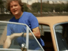 a man in a blue t-shirt is getting out of a car
