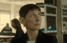 a woman with short hair is standing in front of a shelf and looking up .