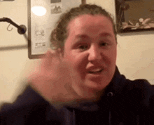 a woman is making a funny face and waving her hand in front of a wall .