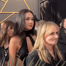 a woman in a black dress is standing next to another woman with blonde hair