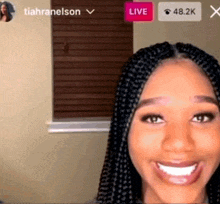 a woman with braids is smiling in front of a window with a live button
