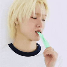 a young man with blonde hair is brushing his teeth with a green stick .