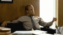 a man in a tie is sitting on a couch in front of a window