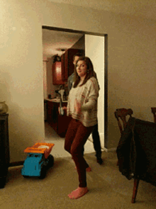 a woman in pink socks is dancing in a living room with a toy truck in the background