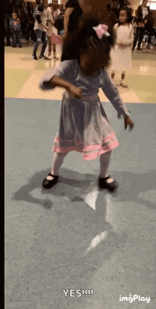 a little girl in a blue and pink dress is dancing in a room .