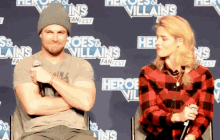 a man and a woman sitting in front of a wall that says heroes and villains fanfest