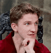 a young man is sitting in a chair with his hand on his chin and looking at the camera .