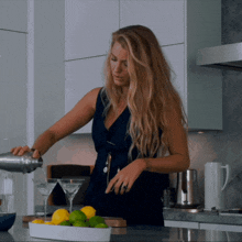 a woman in a blue dress pours a martini into a glass