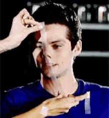 a man in a blue shirt is being taped to another man 's forehead .