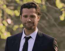 a man in a suit and tie is smiling in front of trees