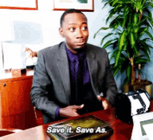a man in a suit sits at a desk with a book that says " save it save as "