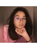 a girl wearing glasses and a pink shirt looks at the camera