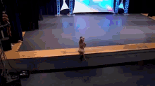a woman is sitting on the edge of a stage in front of a large screen ..