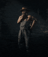 a man in overalls and a hat is smoking a cigarette