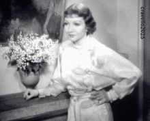 a woman in a white dress stands in front of a vase of white flowers with the year 2025 on the bottom