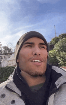 a man wearing a beanie and a jacket is smiling at the camera .