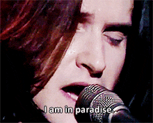 a woman singing into a microphone with the words " i am in paradise " written below her