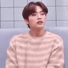 a young boy wearing glasses and a sweater is sitting on a couch .