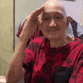 an elderly man with a mustache is wearing a red shirt and making a salute gesture .