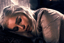 a woman with blonde hair is laying down with her head on her hands