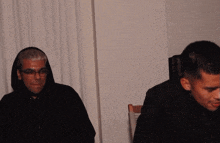 two men are sitting next to each other and one is wearing a hoodie