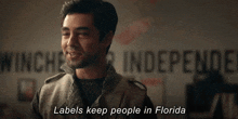 a man is standing in front of a wall that says labels keep people in florida .