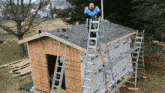 a man standing on a ladder on top of a shed with a roof that has a shingle on it