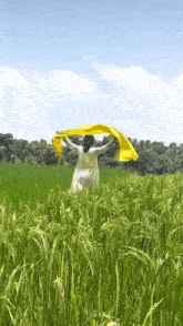 a woman in a white dress is standing in a field of tall grass holding a yellow cloth .