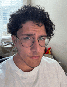 a young man wearing glasses and a white shirt looks at the camera