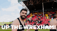 a man with a beard stands in front of a stadium with the words up the wrexham